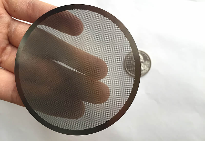 A hand is touching a piece of translucent perforated round filter disc. Under the disc, there is a metal coin.