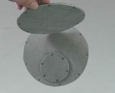 Two circular spot welded filter packs flat on ground and another circular filter disc upright on them.