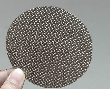 Two fingers hold a single layer filter disc made of stainless steel mesh and without framed edge.
